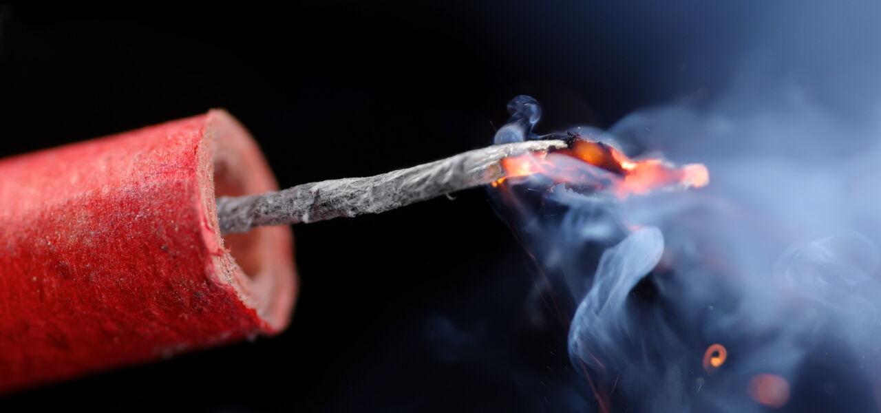 Ein roter Böller mit glühender Zündschnur vor schwarzem Hintergrund