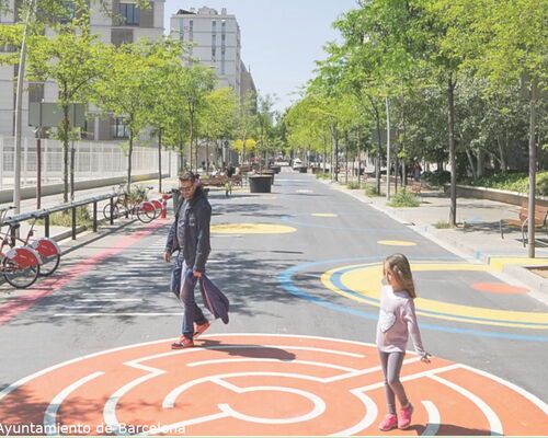 Vater und Kind spielen auf einem aufmarkierten Spiel auf einer Spielstraße in einem Superblock in Barcelona. Links und rechts stehen Straßenbäume