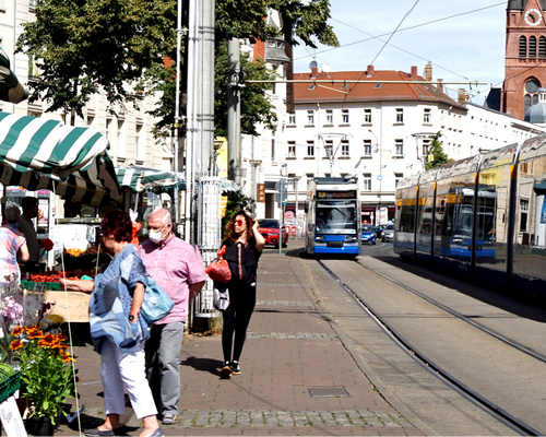 Fußgänger laufen entlang von Markständen. Daneben fährt eine Straßenbahn