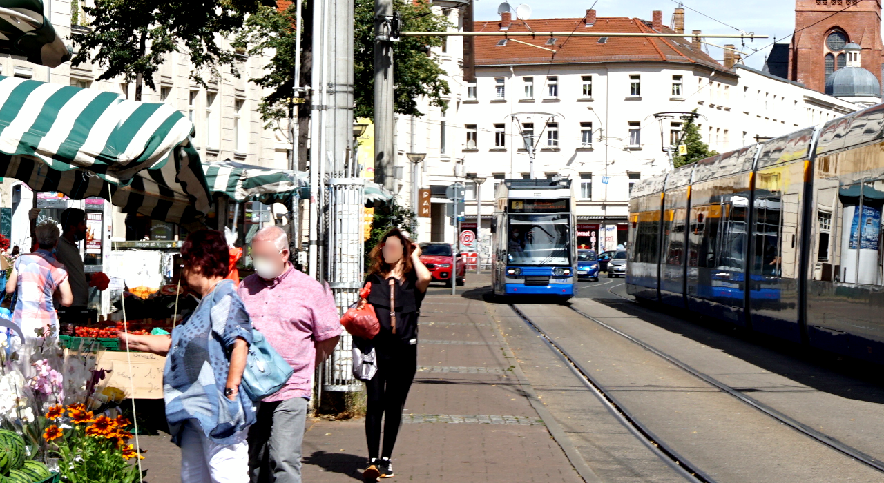 Fußgänger laufen entlang von Markständen. Daneben fährt eine Straßenbahn.