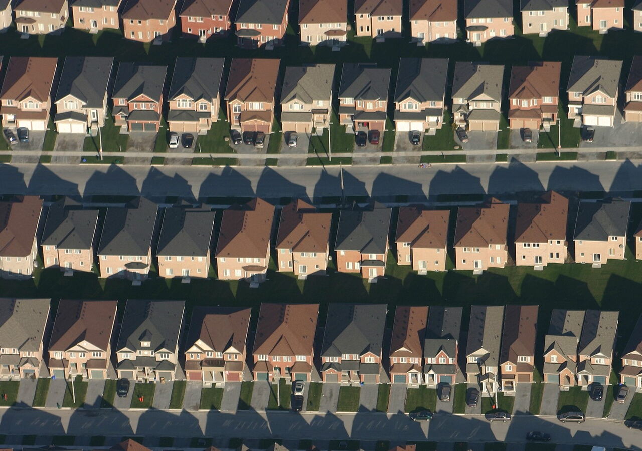 gleich aussehende Einfamilienhäuser reihen sich monoton aneinander. Dazwischen eine Erschließungsstraße und Hauseinfahrten mit Autos