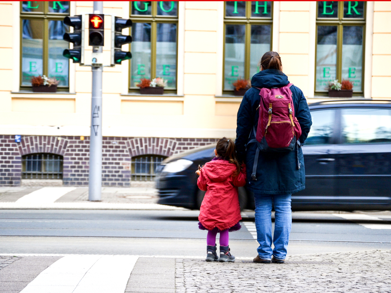 Frau und Kind stehen an einer roten Ampel