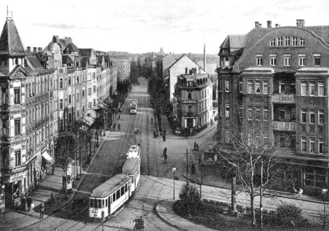 Historische Schwarzweißaufnahme einer Stadtstraße mit Straßenbahnen und Gebäuden.