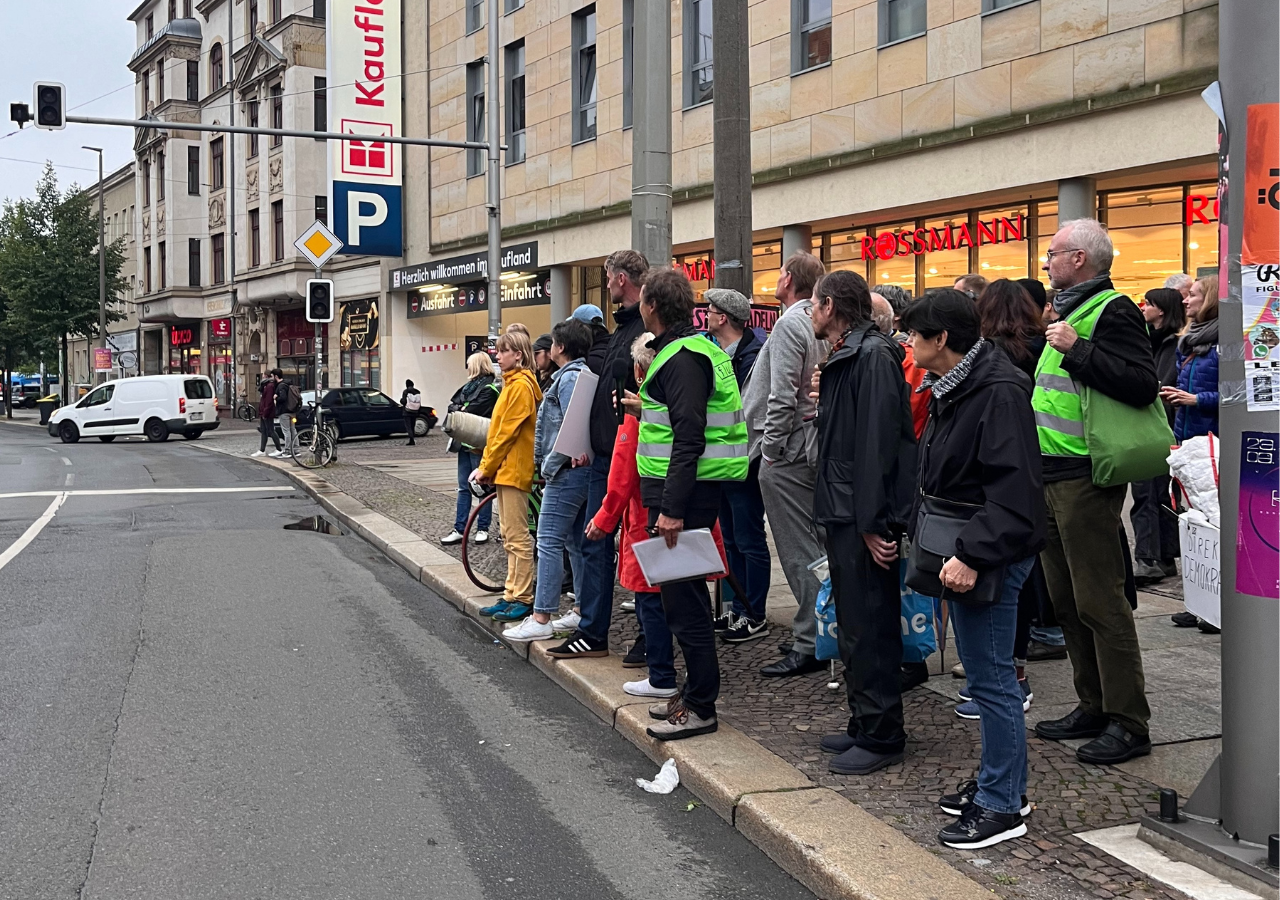 Eine Gruppe von Fussgänger:innen wartet vor dem Kaufland darauf, die Dresdner Straße zu überqueren. Was sehr schwierig ist.