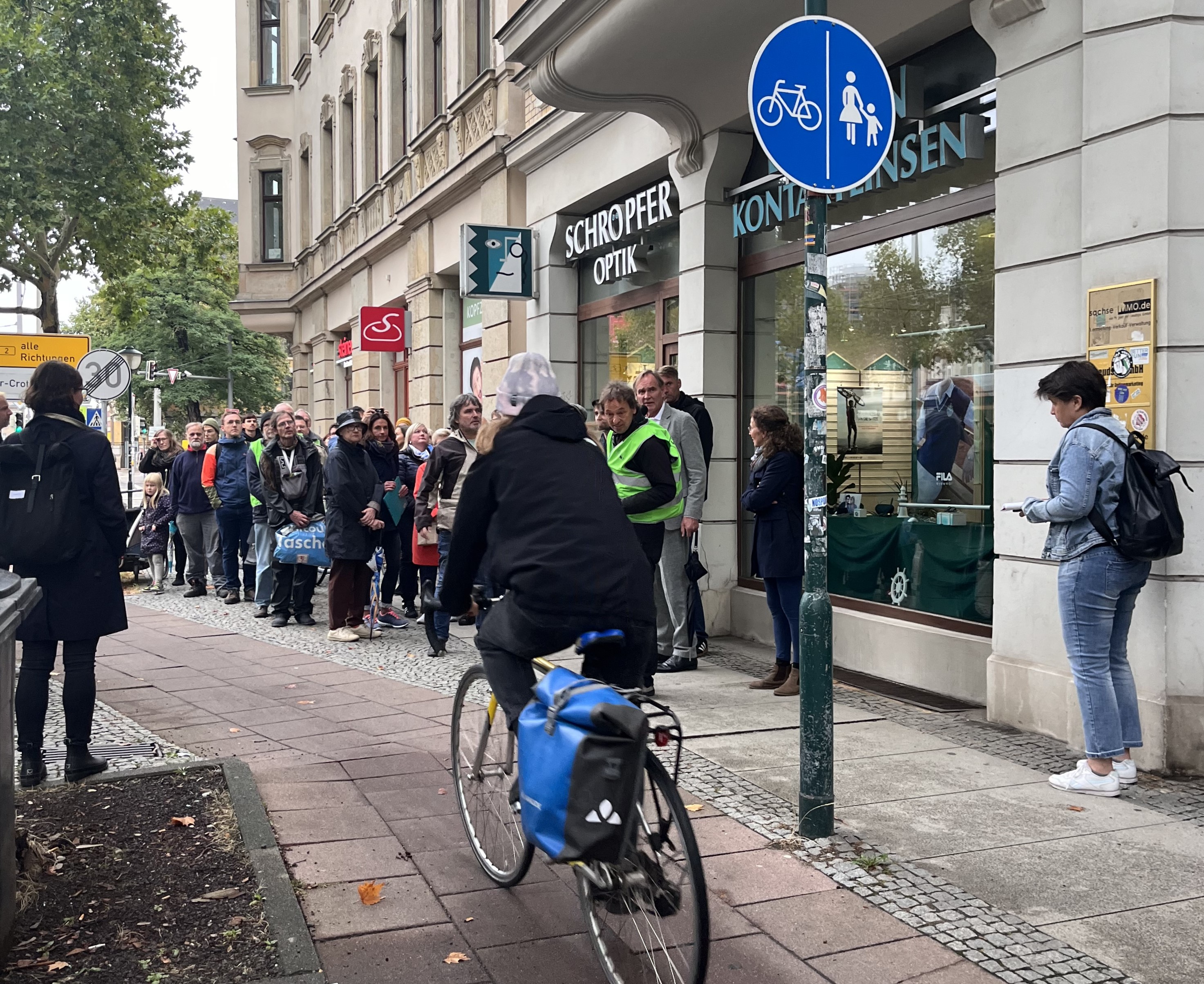 Das Bild zeigt, wie sich auf der engen Geschäftsstraße Prager Straße Fuss- und Radverkehr in die Quere.  Es ist ein Radfahrer zwischen Fussgänger:innen zu sehen.