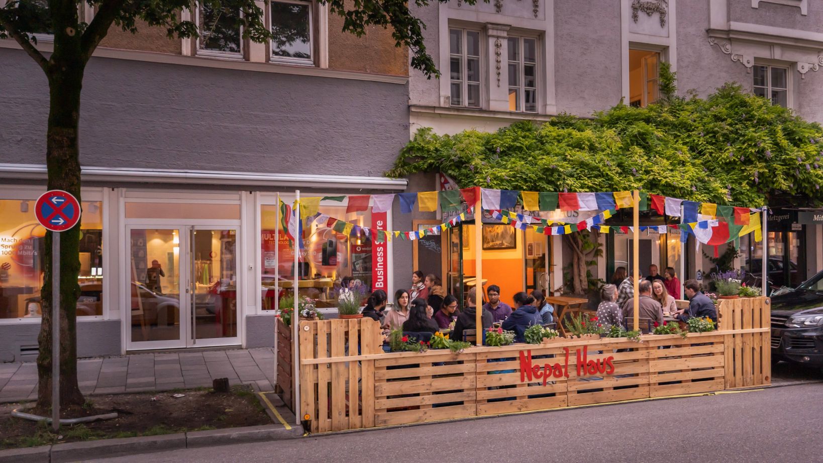 Der Schanigarten "Nepal Haus" mit Gästen in München. Mit bunten Blumenkästen und Wimpeln. Bald auch in Leipzig