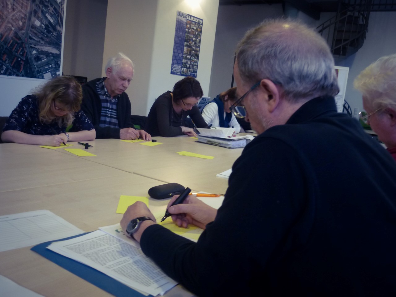 Menschen sitzen an einem Tisch und lesen Maßnahmenblätter